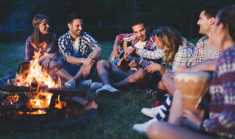 Happy friends playing music and enjoying bonfire